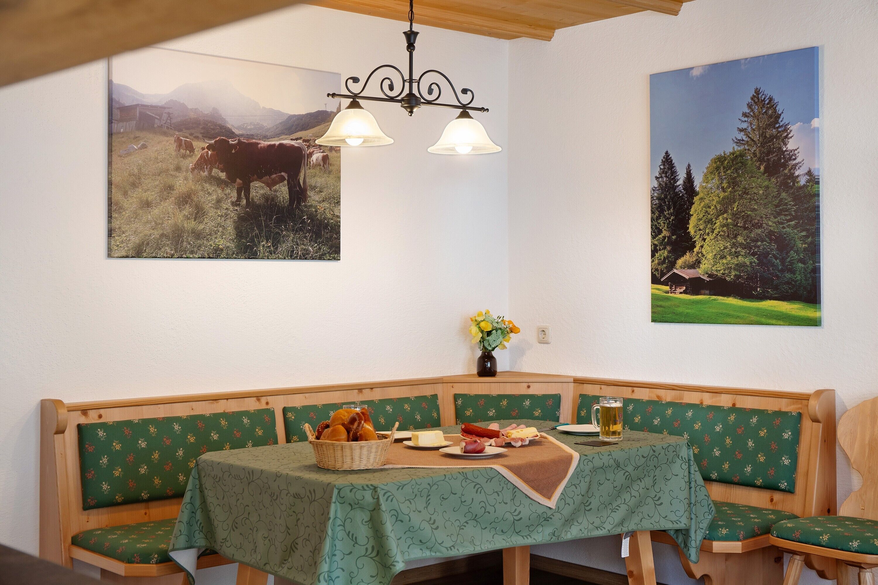 A dining area with a wooden bench, a table with a green tablecloth, and two wall-mounted light fixtures.
