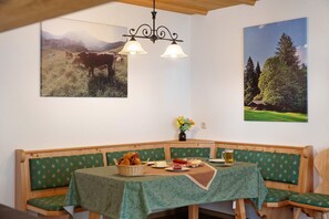 Un coin repas avec un banc en bois, une table recouverte d’une nappe verte et deux appliques murales.
