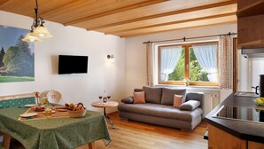 A cozy room with a wooden ceiling, a sofa, a dining table with a green tablecloth, a television, and a window with curtains. - Apartment 'Ferienwohnung Waxensteinblick' with Mountain View, Balcony and Wi-Fi (Grainau)