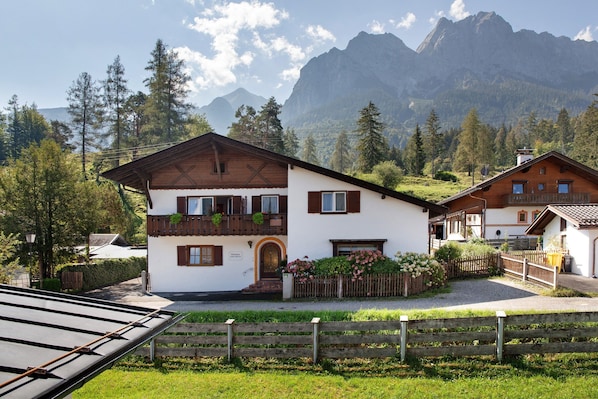 Un chalet à deux étages doté d’un balcon, entouré d’une cl ôture en bois, et situé dans un cadre montagneux.