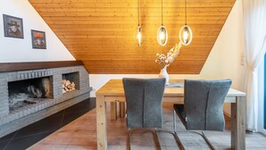 Un comedor con techo de madera, chimenea y dos sillas grises.