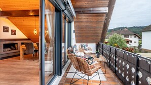 Un balcón con mobiliario de mimbre, una puerta de cristal y vistas del entorno.