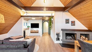 Una sala de estar acogedora con chimenea, un sofá, un televisor y techo de madera.
