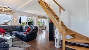 A modern living room with a black leather sofa, wooden staircase, and a dining area in the background. - Holiday Home 'Sonja' with Private Terrace, Wi-Fi and Air Conditioning (Lichtenwalde)