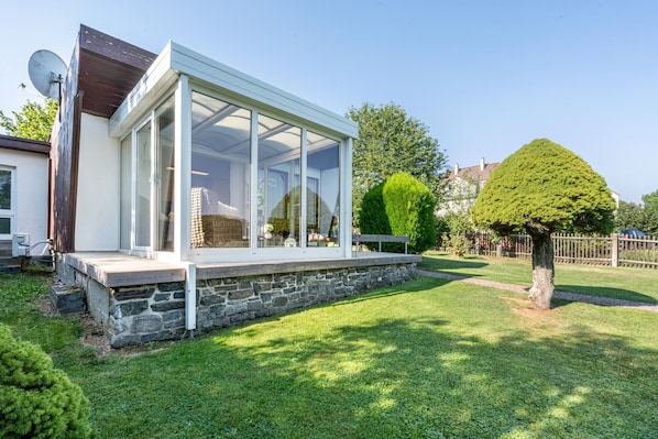 Una casa moderna con un porche de cristal, base de piedra y césped cuidado.
