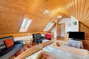 Une pièce confortable de style loft, avec un plafond en bois, un canapé, un lit, une télévision et un fauteuil rouge.