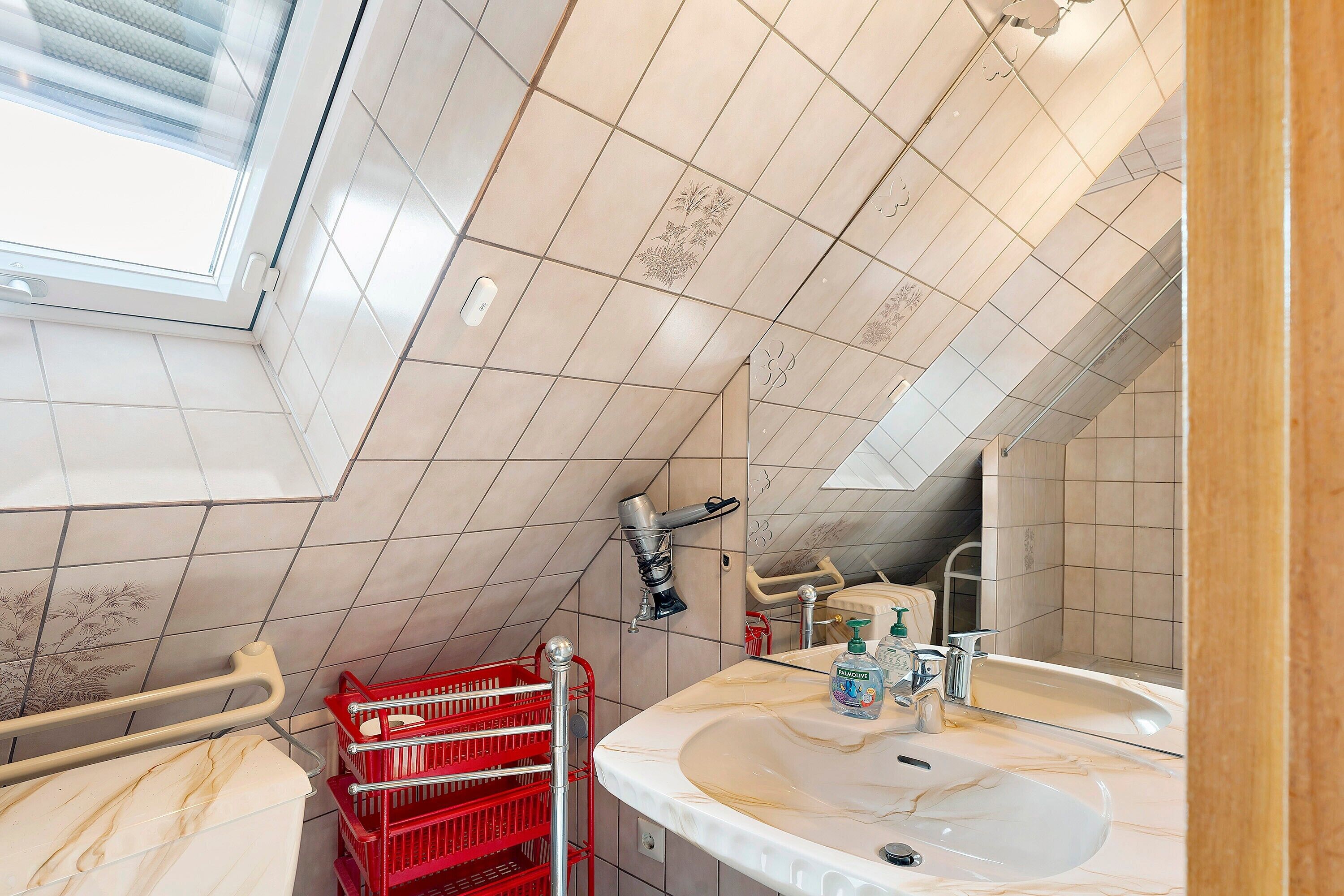 A bathroom with a skylight, a sink with a mirror, and a red basket.