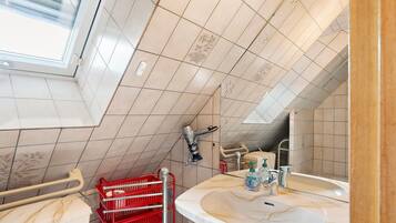 A bathroom with a skylight, a sink with a mirror, and a red basket.
