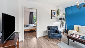 Un salon moderne comprenant un téléviseur à écran plat, un canapé, un fauteuil à motifs, une table basse et un lampadaire.