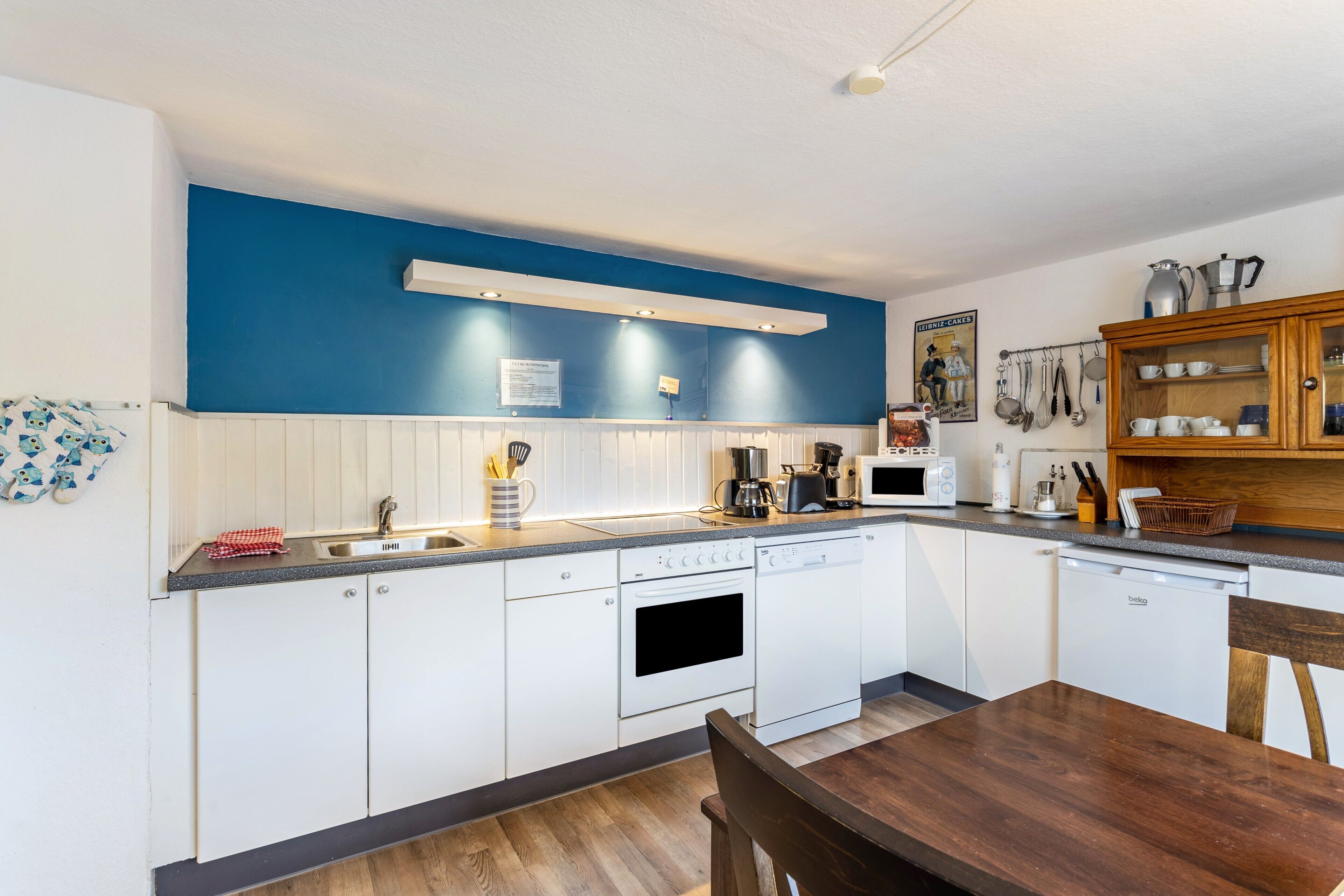 Una cocina moderna con armarios blancos, una pared de acento azul y una mesa de comedor de madera.