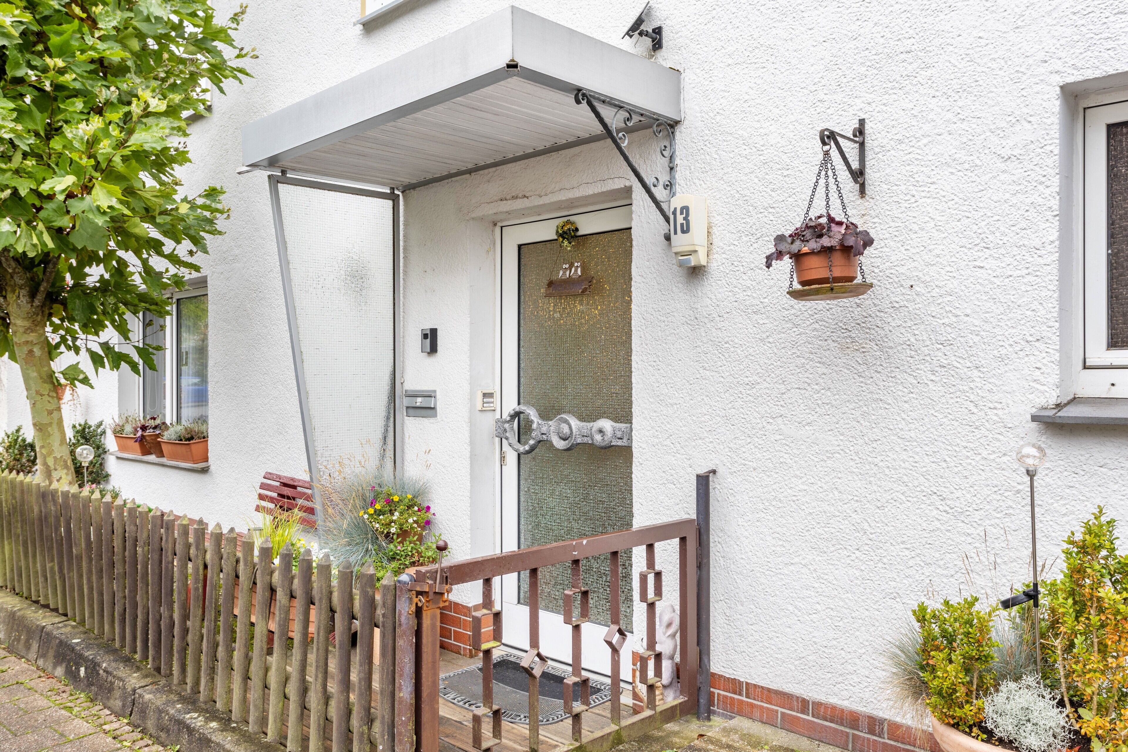 A white building with a wooden fence, a door with a number plate, and a hanging flower pot.