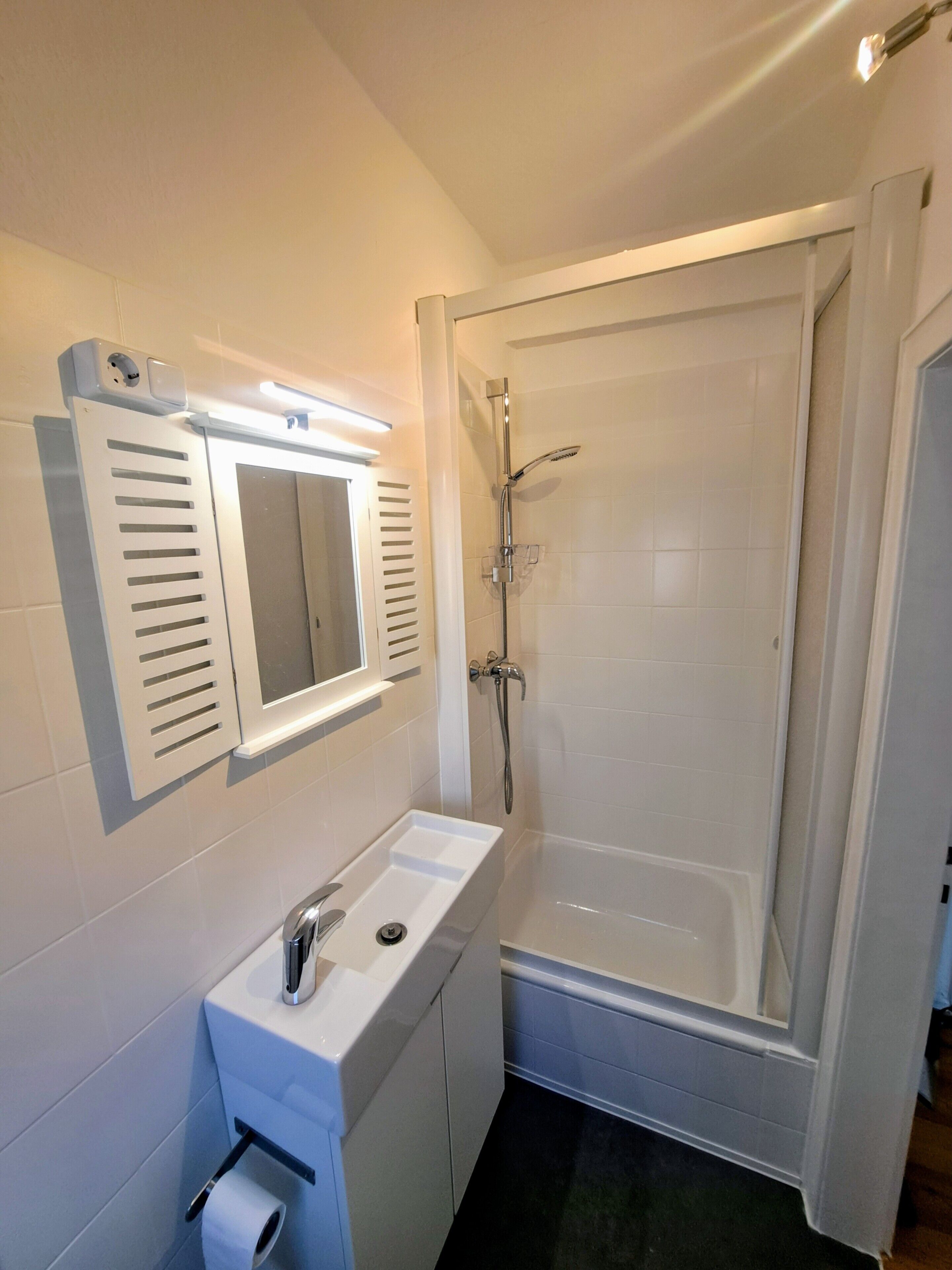 Une salle de bain avec un lavabo blanc, un miroir et une douche.