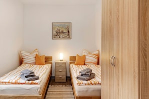 A room with two beds, a nightstand, a lamp, a painting on the wall, and a wooden wardrobe. - Apartment 'Innenstadt Quartier' (Neuruppin)