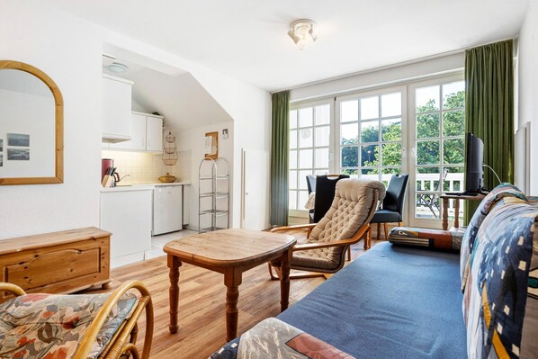 A spacious living area with a sofa, wooden table, and chairs, a kitchen in the background, and a large window with curtains. - Apartment 'Haus Baltic - Ferienwohnung 29' with Balcony and Wi-Fi (Sellin)