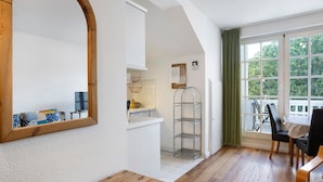 Une pièce avec une table en bois, un miroir, un mur blanc, une fenêtre donnant sur un paysage et une chaise.