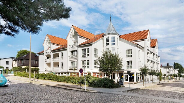 Un grand bâtiment blanc coiffé d’un toit recouvert de tuiles rouges, doté de nombreux balcons et d’une tour d’angle.