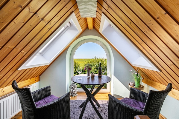 Une pièce avec un plafond en pente, une table ronde entourée de chaises et une vue sur la verdure par une fenêtre en arc de cercle.