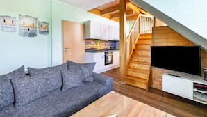 Ein modernes Wohnzimmer mit grauem Sofa, einer Holztreppe und einem Flachbildfernseher auf einem weißen Standfuß.