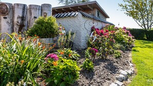 Ein rustikales Gebäude mit einer Steinaußenwand, umgeben von einem gepflegten Garten mit verschiedenen Pflanzen und Blumen.