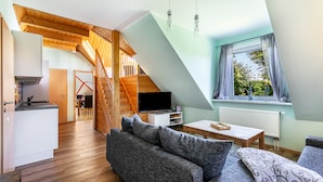 Ein modernes Loft-Zimmer mit Holztreppe, einer Couch, einem Fernseher und einem Fenster mit Vorhängen.