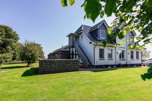 Une maison à deux étages, dotée d’un toit en pente, d’un mur en pierre et d’une pelouse bien entretenue.