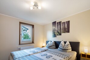 A bedroom with a bed, a window, a radiator, a nightstand, and wall art.