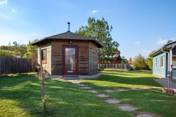 A small wooden cabin with a red door, surrounded by a well-maintained lawn and a wooden fence.