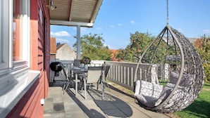 Eine überdachte Terrasse mit Hängestuhl, Grill und Esstisch.