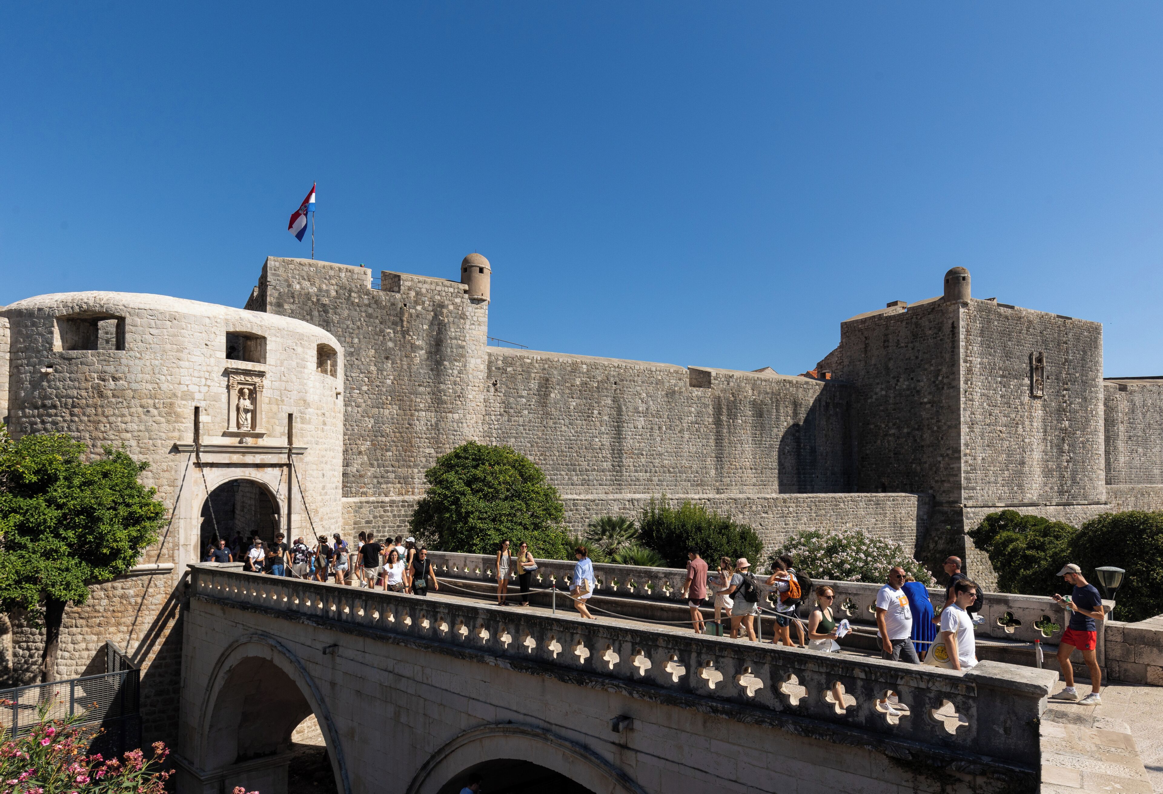 Una fortaleza de piedra histórica con un puente que la conecta, rodeada de turistas.