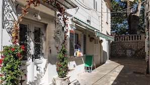 A narrow street with a white building featuring a green awning, a small outdoor seating area, and a stone wall. - Room-seistanca Lux - Old City Entrance D (Dubrovnik)