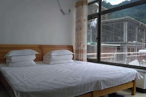 A bed with white bedding, a wooden headboard, and a window with a view of a building and mountains. - Beijing Sunshine Courtyard Farmhouse (Beijing)