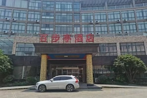 A hotel entrance with a modern design, featuring a prominent name sign above the entrance and a white car parked in front. - Baibuting Hotel (Haiyan)