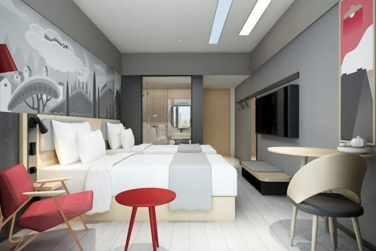A modern hotel room with a large bed, a desk, a chair, and a TV.