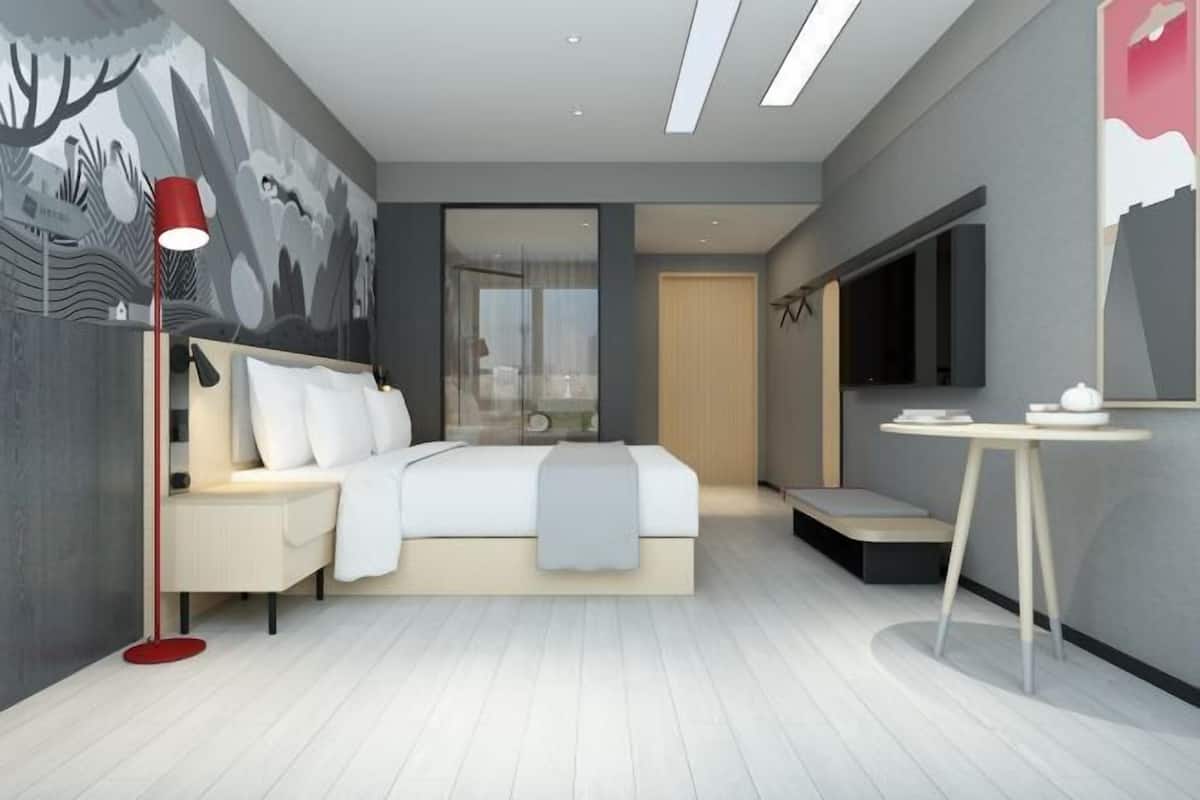 A modern bedroom with a bed, bedside table, lamp, and a large window.