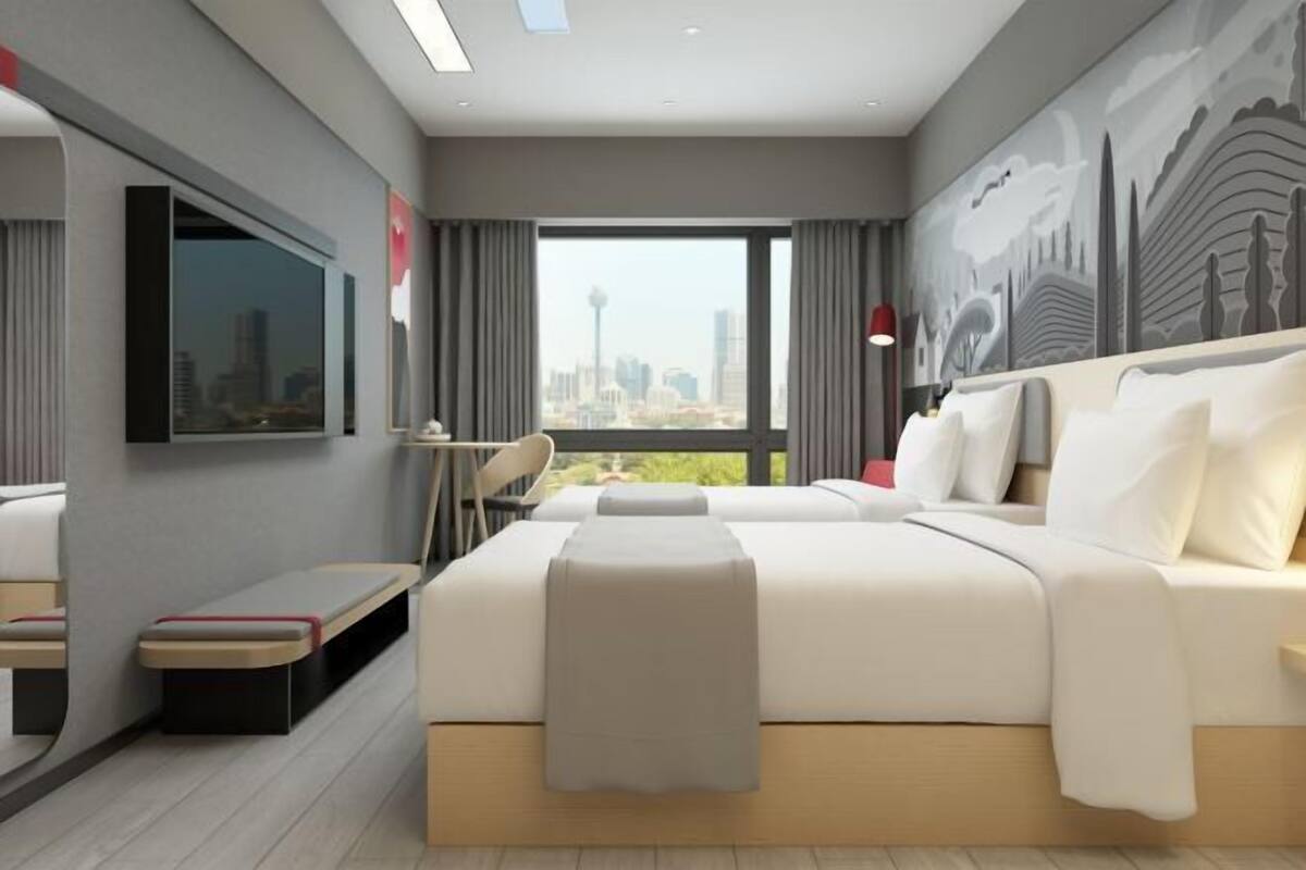 A modern hotel room with a large bed, a desk, a chair, a TV mounted on the wall, and a city view.