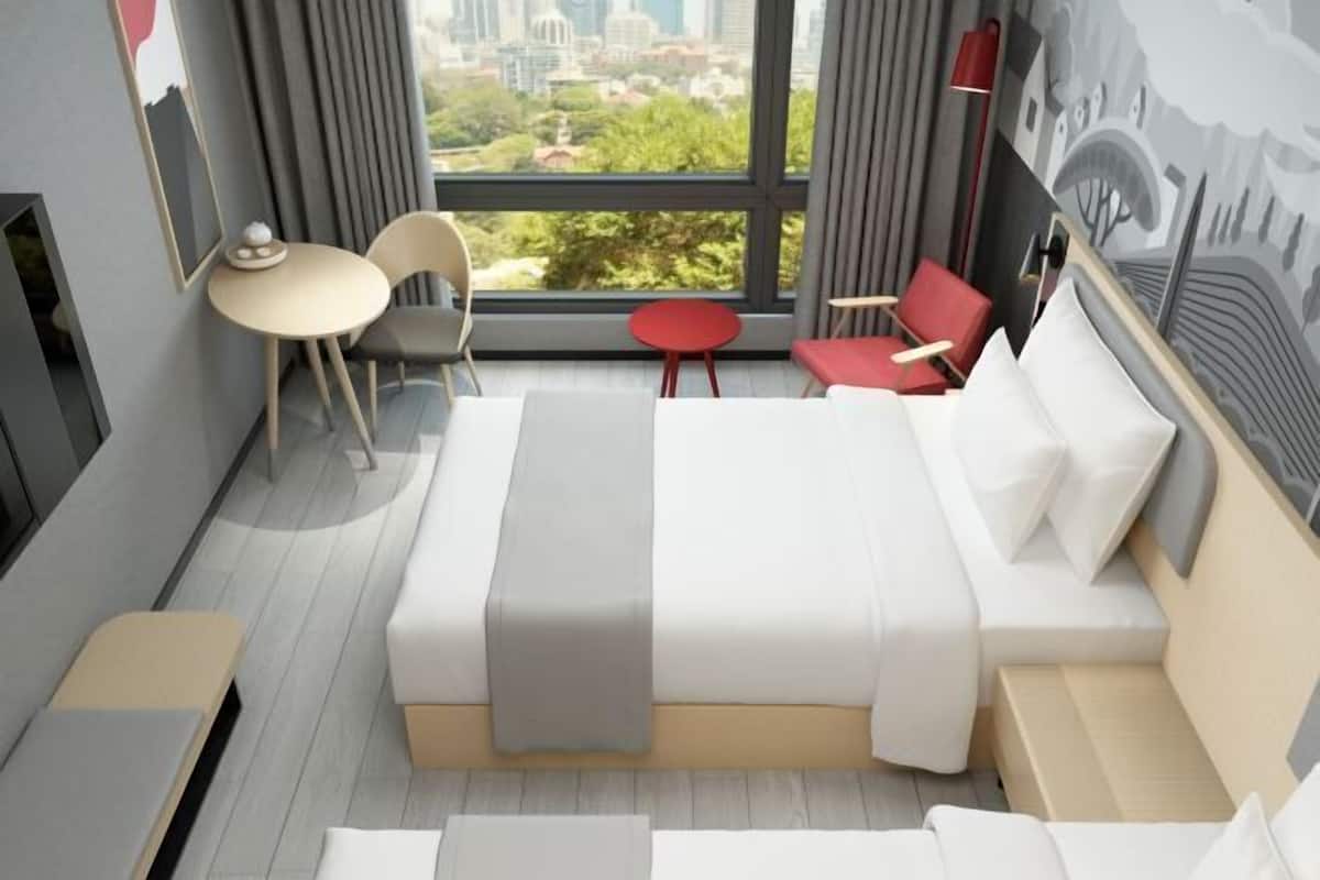 A modern hotel room with a large bed, a small round table, two chairs, a red chair, and a view of the city.