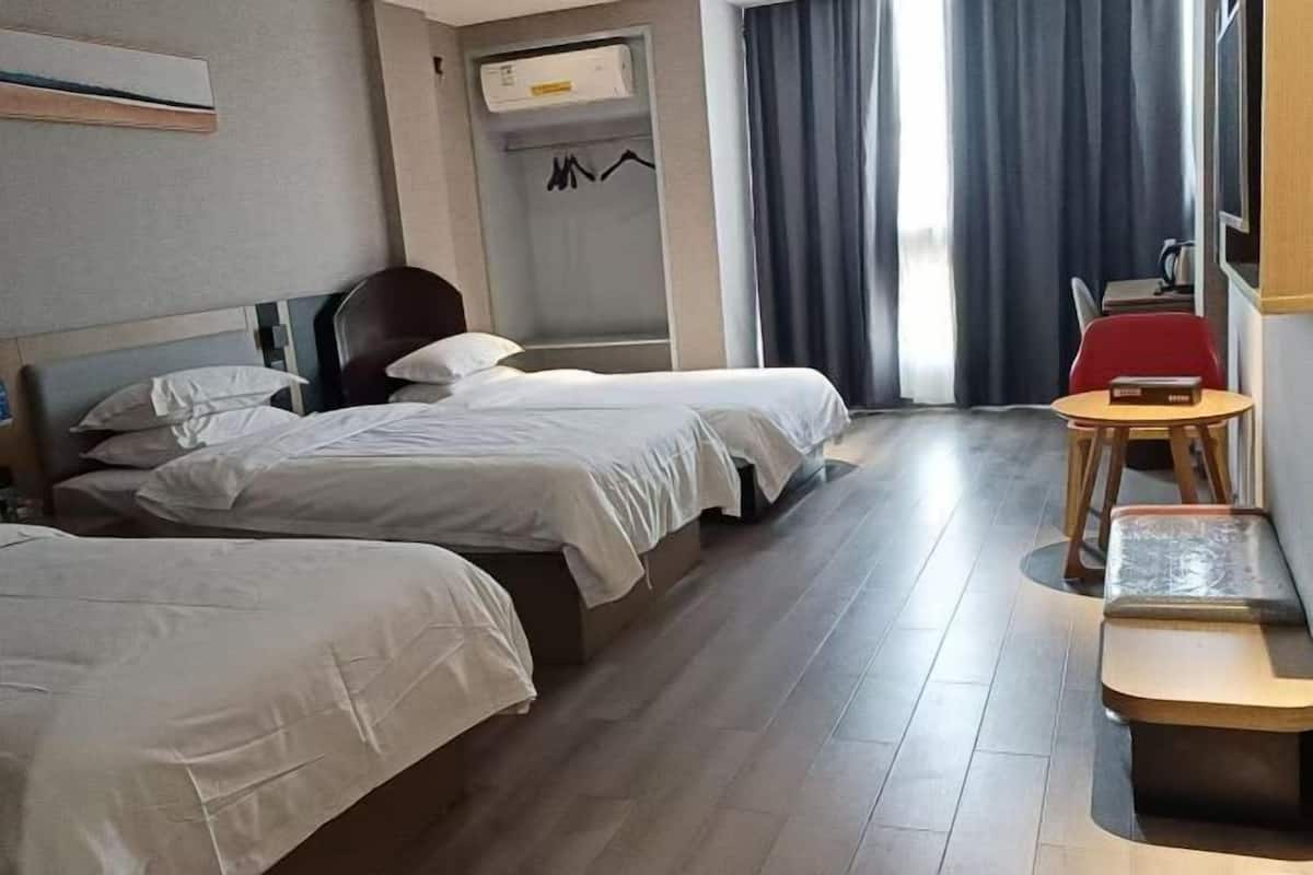 A hotel room with two beds, a small table, a bench, a coat rack, and a window with curtains.