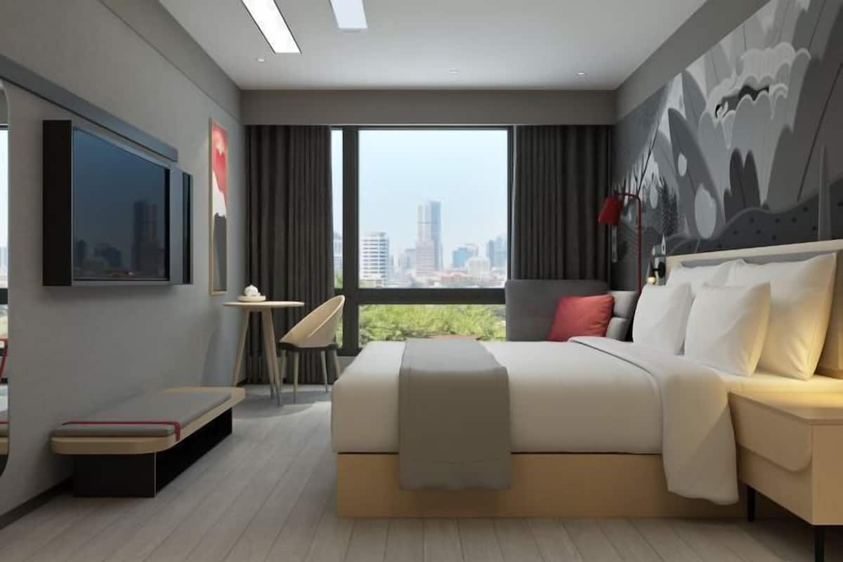 A modern hotel room with a large bed, a TV, a small table, and a chair.