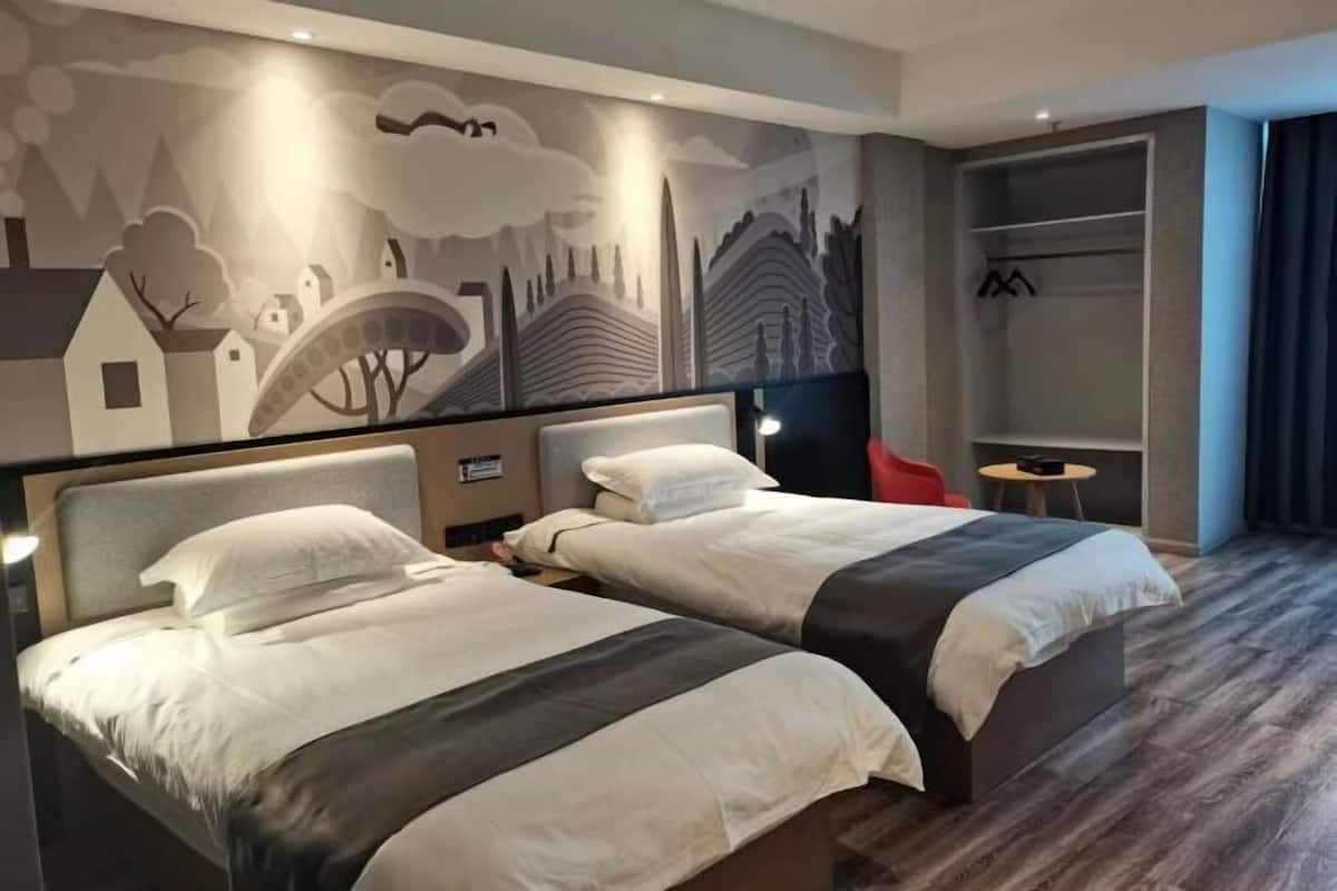 A hotel room with two beds, a mural on the wall, a red chair, and a walk-in closet.