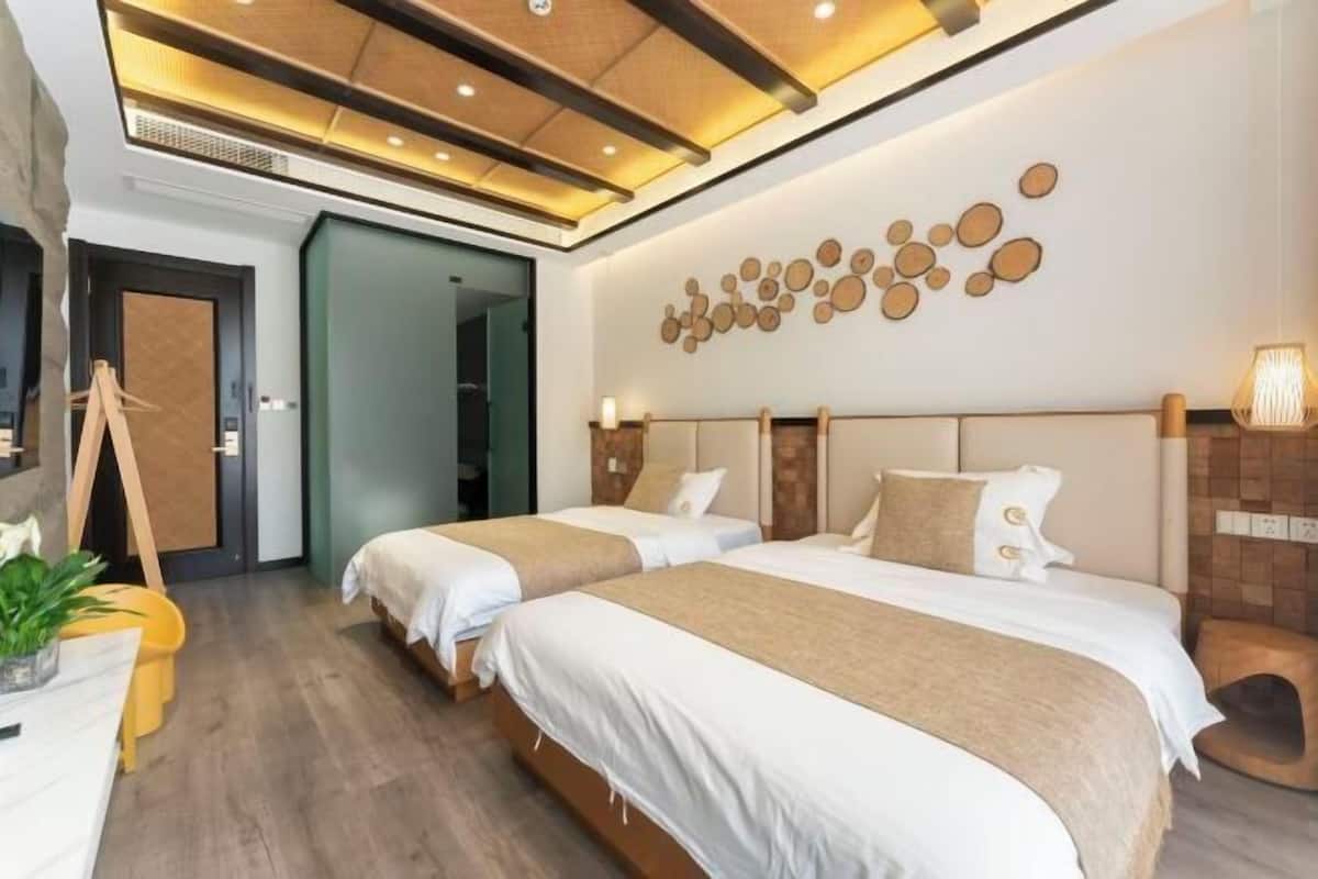 A hotel room with two beds, a wooden floor, a wall with circular decorations, and a ceiling with recessed lighting.