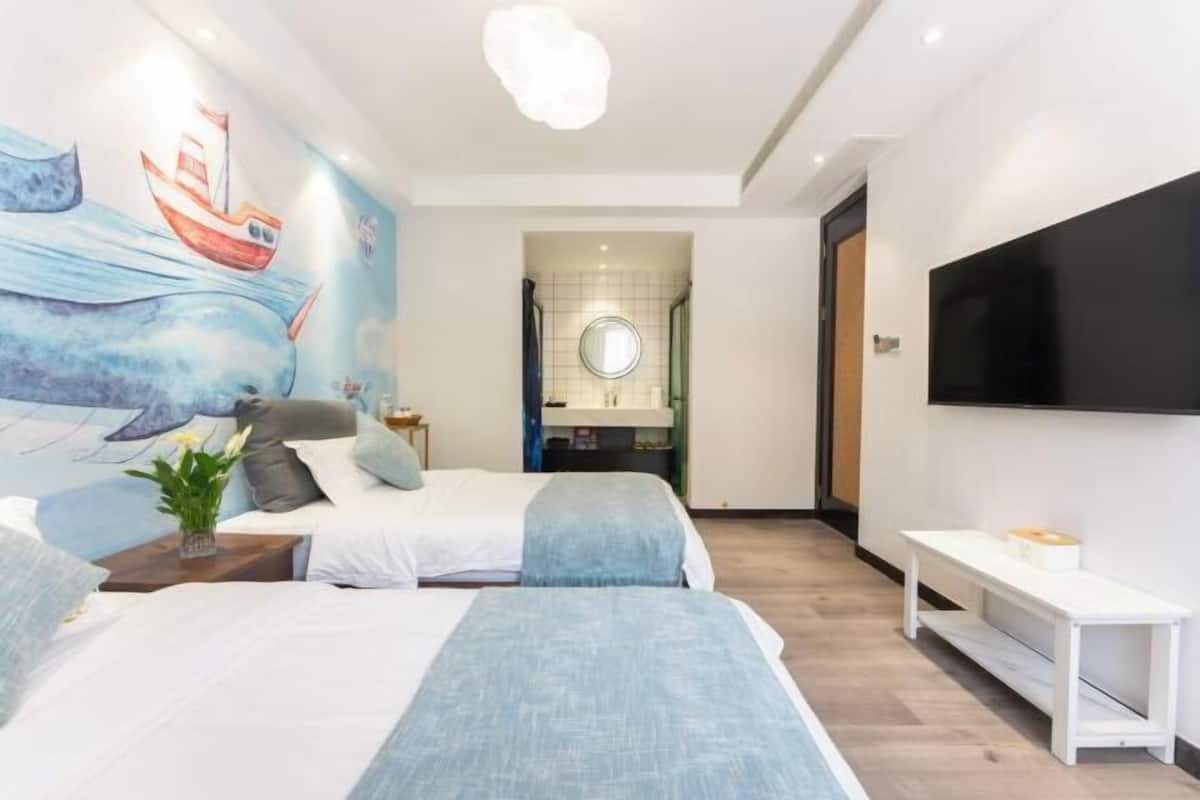 A modern hotel room with two beds, a large TV, and a mural of a ship on the wall.