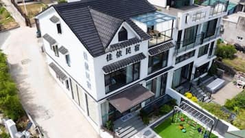 A multi-story building with a flat roof, large windows, and a visible outdoor area with greenery.