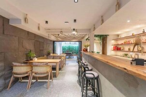 Interior de restaurante con una barra larga, taburetes y una zona de estar con mesas y sillas.