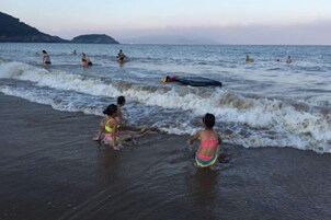 Una playa con gente en el agua y en la orilla.