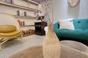 Una sala de estar con un sofá color turquesa, una mesa de centro de madera, un sillón amarillo y una estantería con libros y objetos decorativos.