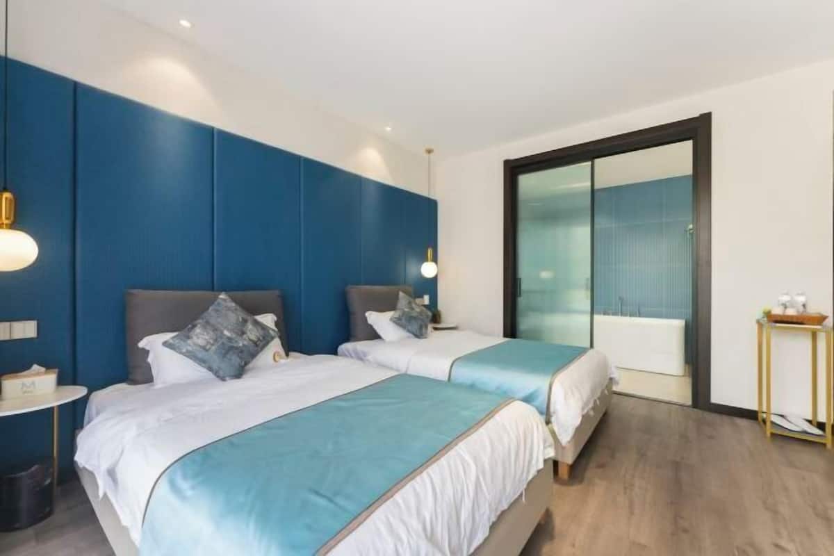 A modern hotel room with two beds, a large mirror, and a small table with a lamp.