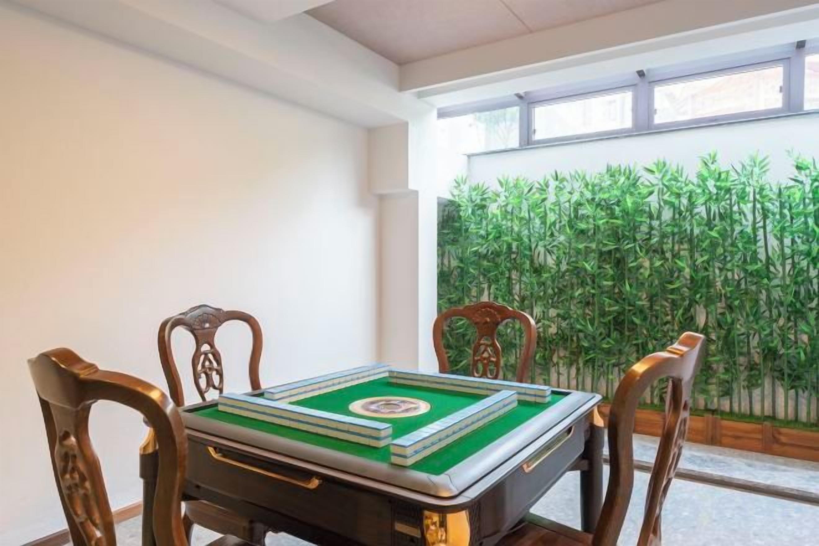 A room with a table set for a game, wooden chairs, and a view of greenery through a window.