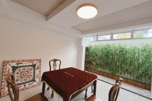 Una habitación con una mesa de comedor, sillas, un tapete estampado y vistas a plantas de bambú a través de una ventana.