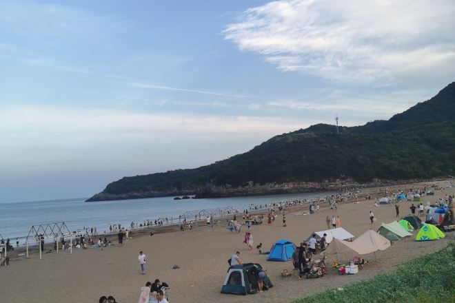 A beach with tents and people, a clear sky, and a hilly landscape in the background.
