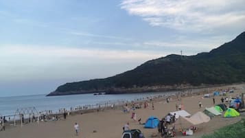 A beach with tents and people, a clear sky, and a hilly landscape in the background.
